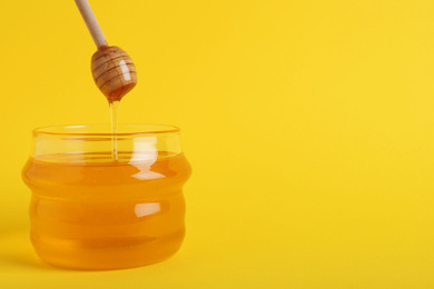 Photo of Jar with organic honey and dipper on yellow background. Space for text