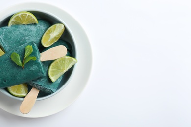 Photo of Bowl with delicious spirulina popsicles and lime slices on white background, top view