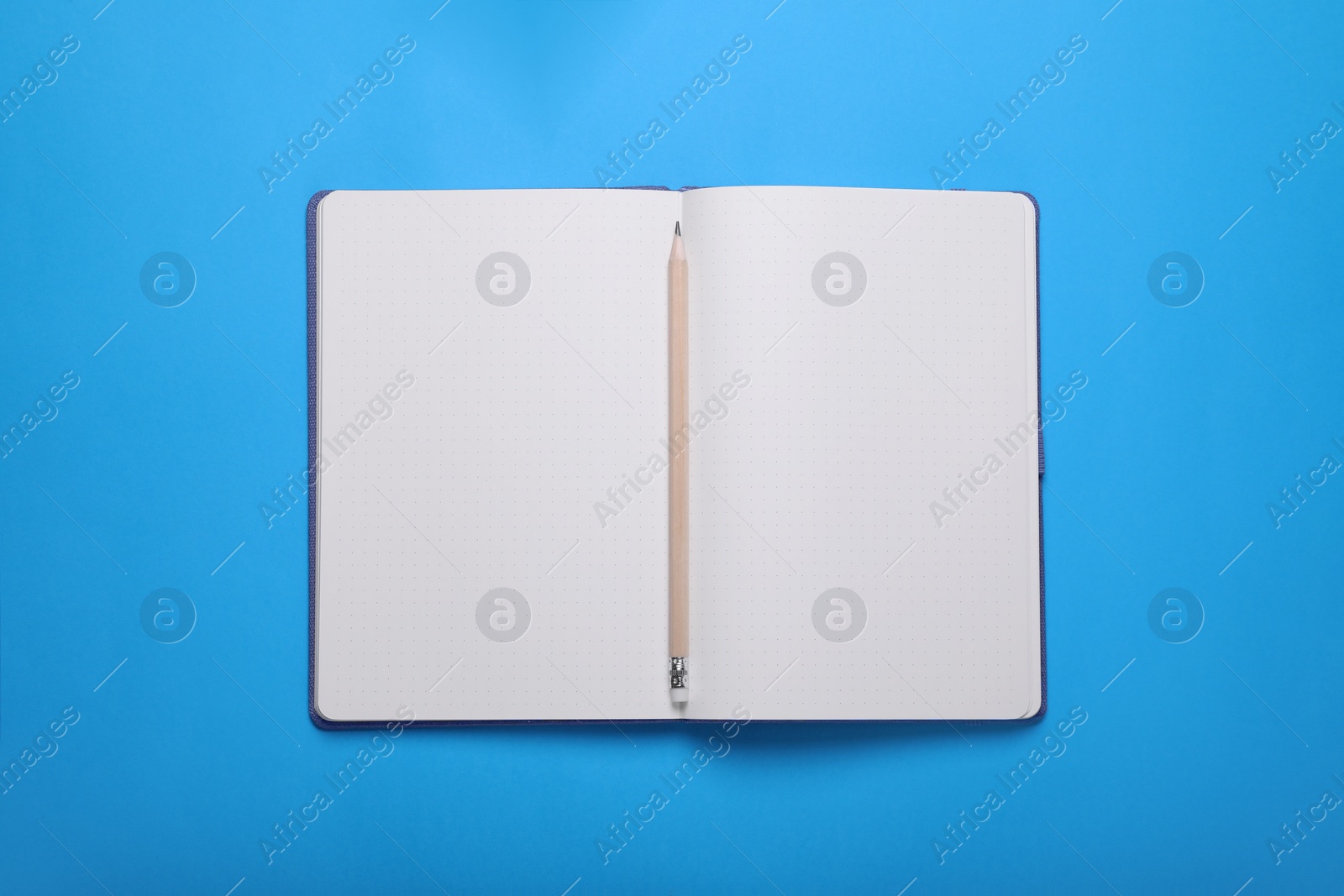 Photo of Open notebook and pencil on light blue background, top view