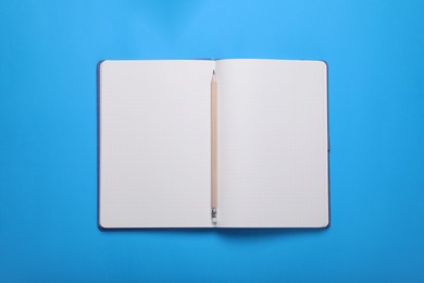 Open notebook and pencil on light blue background, top view