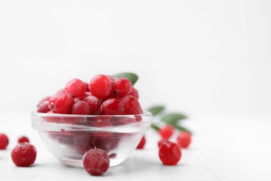 Photo of Frozen red cranberries in bowl on white table, closeup. Space for text