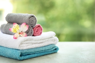 Stack of clean towels with flower on table against blurred background. Space for text
