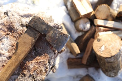 Photo of Metal axe on wooden log and pile of wood outdoors on sunny winter day, top view. Space for text