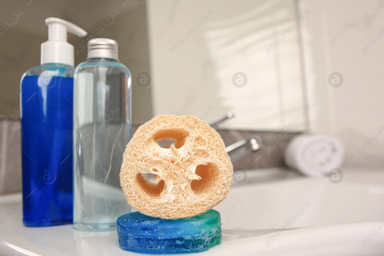 Photo of Loofah sponge and cosmetic products on sink in bathroom, space for text