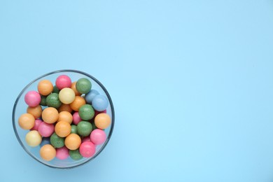 Photo of Bowl with many bright gumballs on light blue background, top view. Space for text