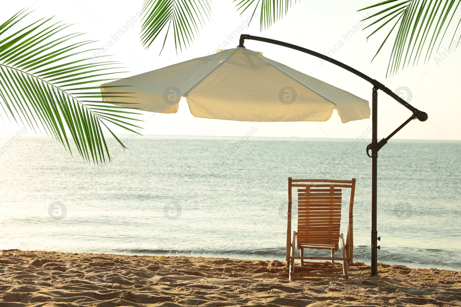 Image of Wooden sun lounger and outdoor umbrella on sandy beach. Summer vacation