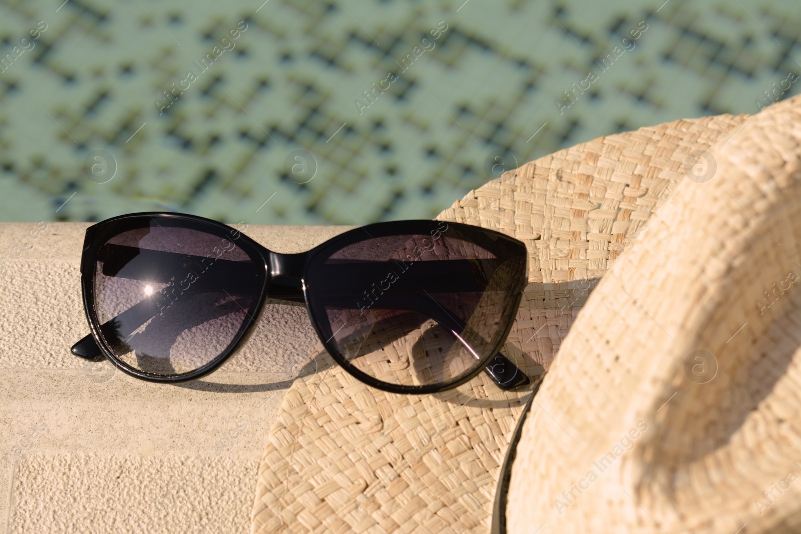 Photo of Stylish hat and sunglasses near outdoor swimming pool on sunny day, closeup