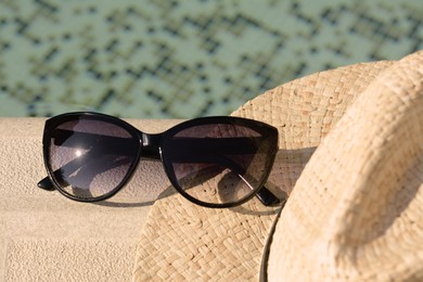 Photo of Stylish hat and sunglasses near outdoor swimming pool on sunny day, closeup