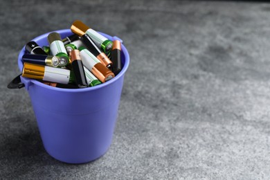 Image of Used batteries in bucket on grey table, space for text