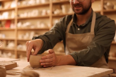 Photo of Clay crafting. Man making bowl at table in workshop, closeup