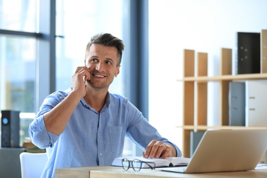 Photo of Male business trainer talking on phone while working with laptop in office