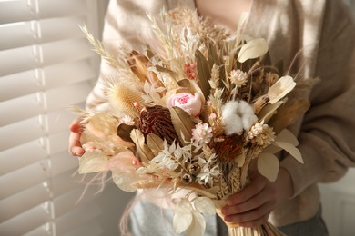 Photo of Woman holding beautiful dried flower bouquet near window at home, closeup