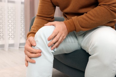 Man suffering from knee pain on sofa indoors, closeup