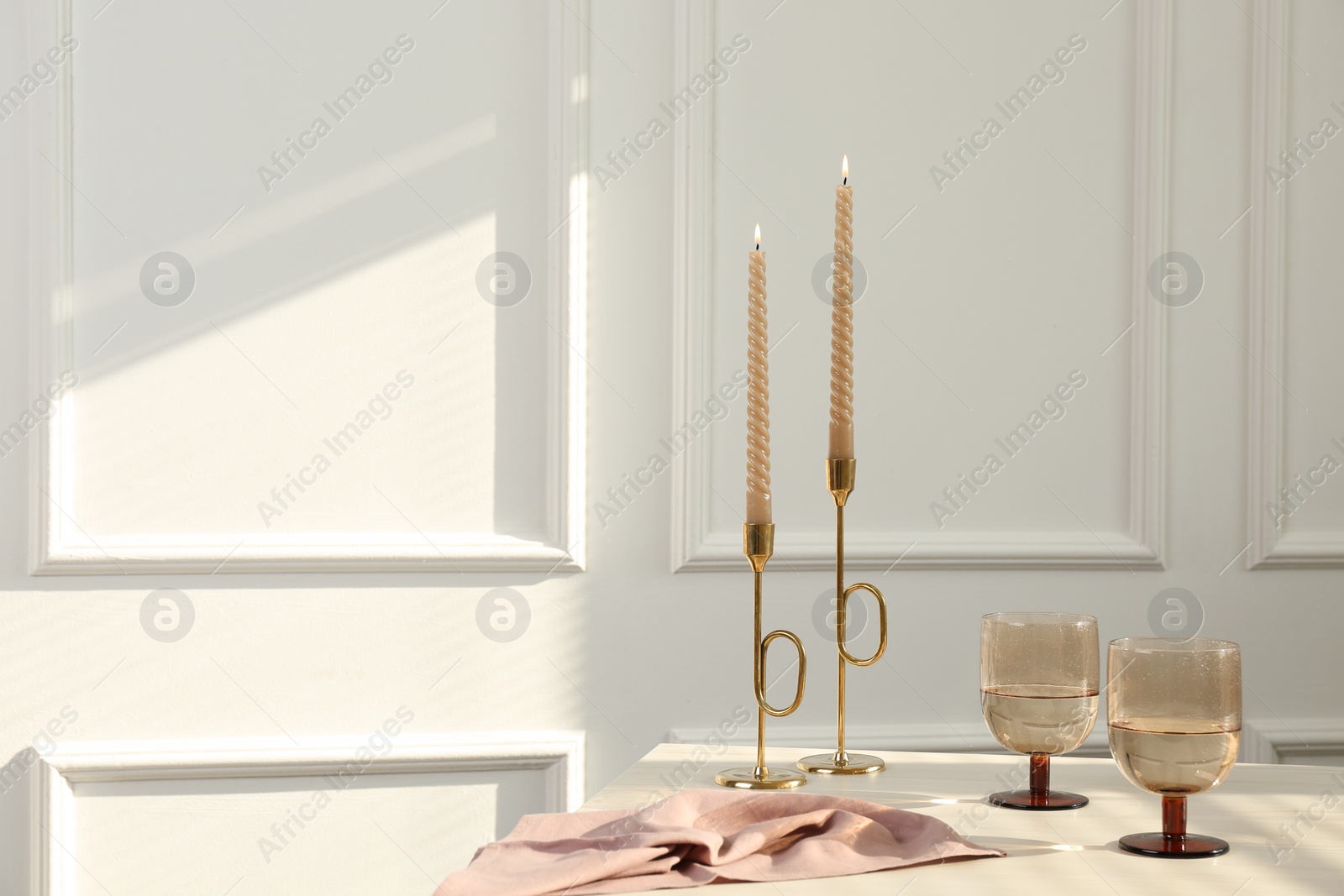 Photo of Glasses of wine near burning candles on white table indoors, space for text