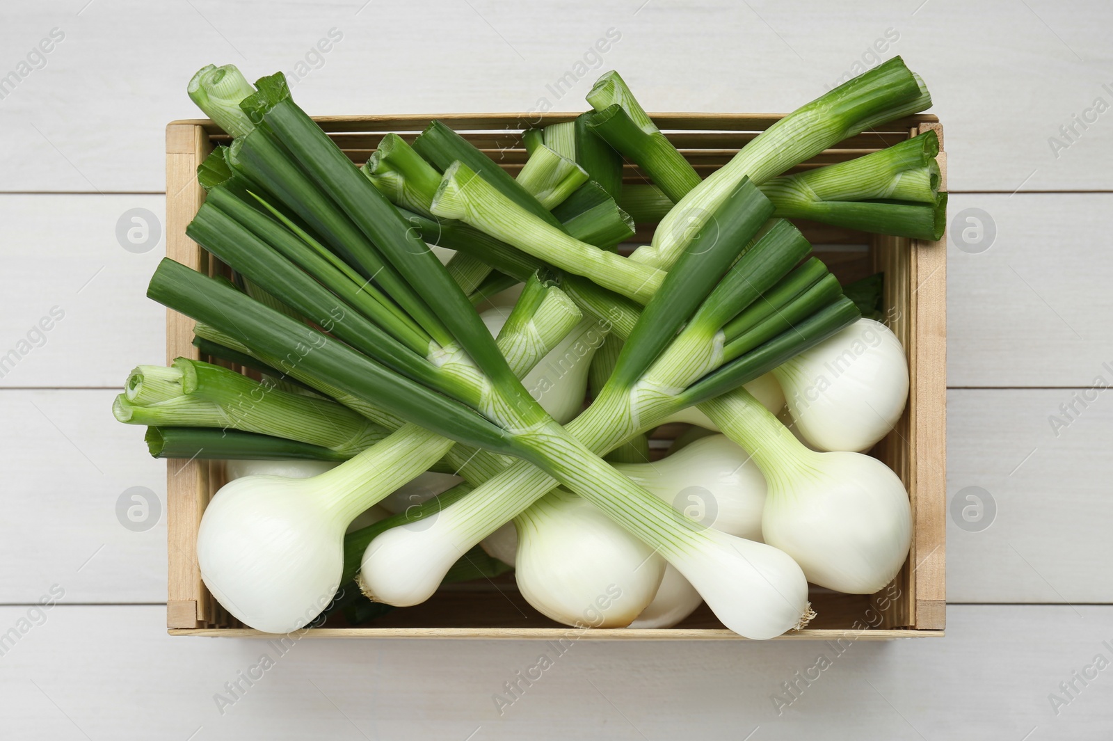 Photo of Crate with green spring onions on white wooden table, top view