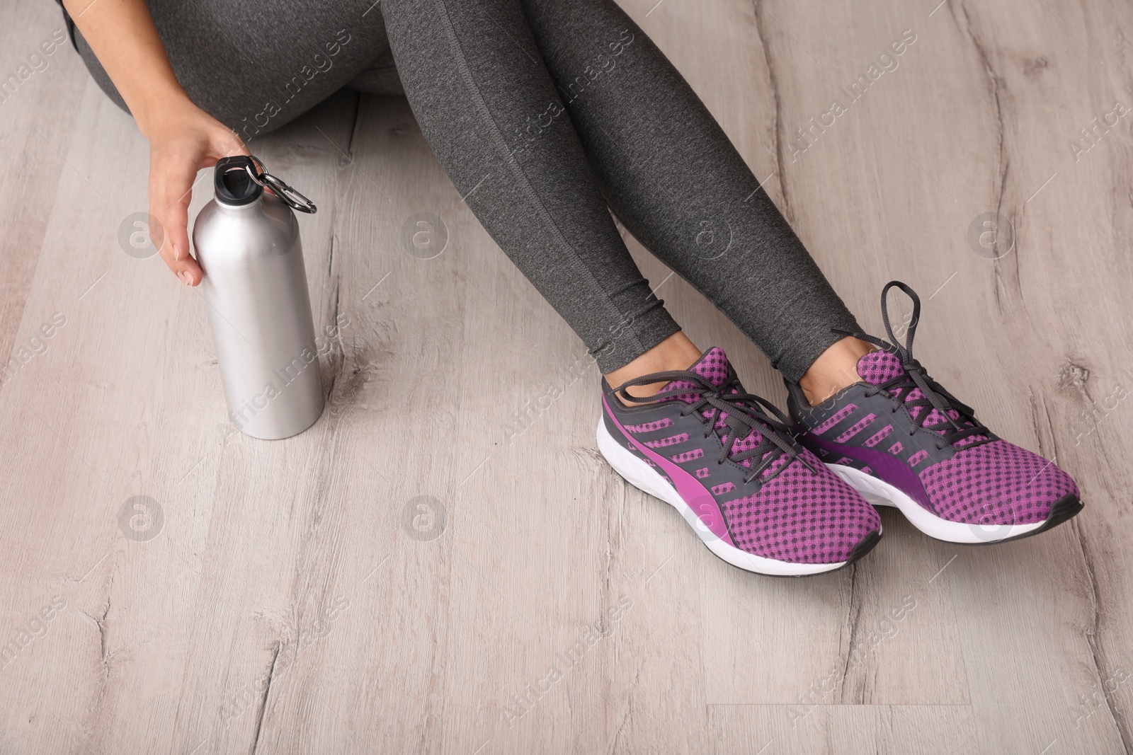 Photo of Woman in sportswear with bottle of water sitting on floor indoors