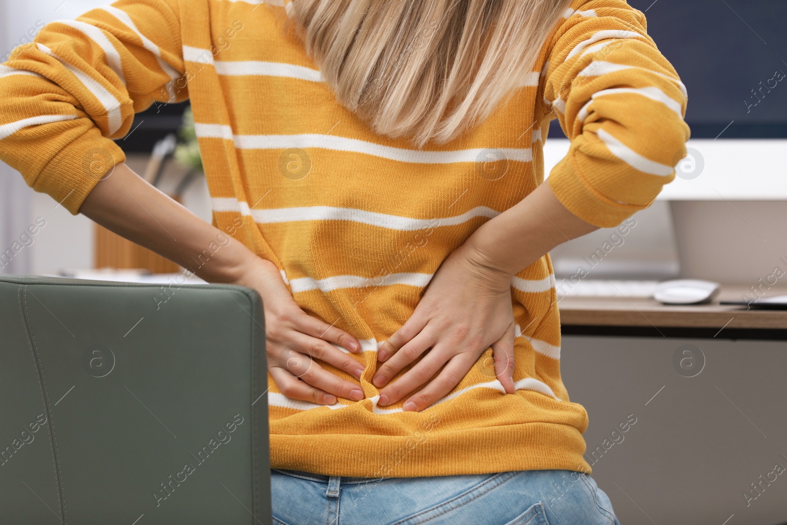 Photo of Young woman suffering from back pain in office, closeup