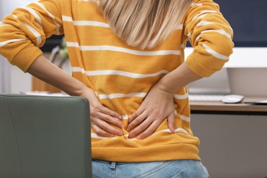 Young woman suffering from back pain in office, closeup