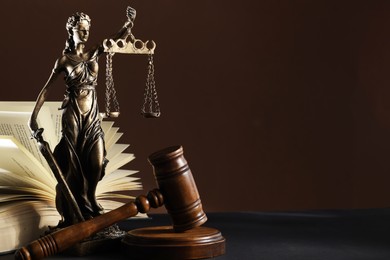 Statue of Lady Justice near gavel and open book on dark table, space for text. Symbol of fair treatment under law