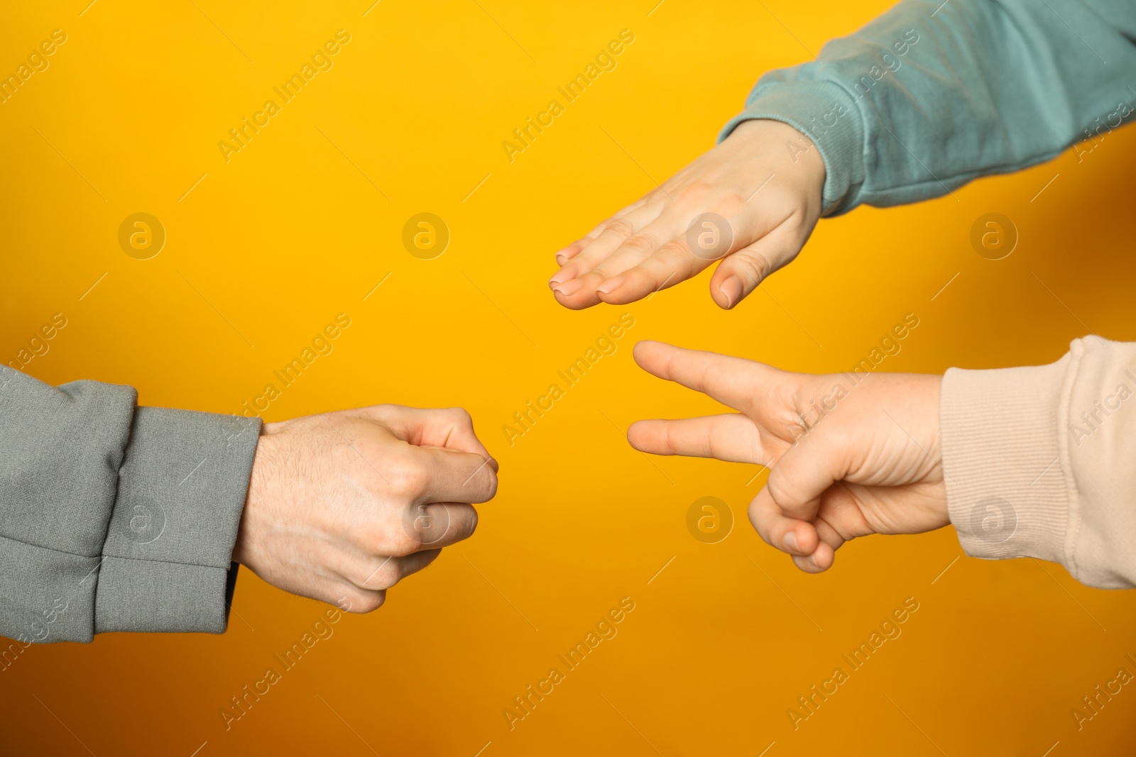 Photo of People playing rock, paper and scissors on orange background, closeup