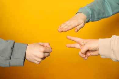 People playing rock, paper and scissors on orange background, closeup