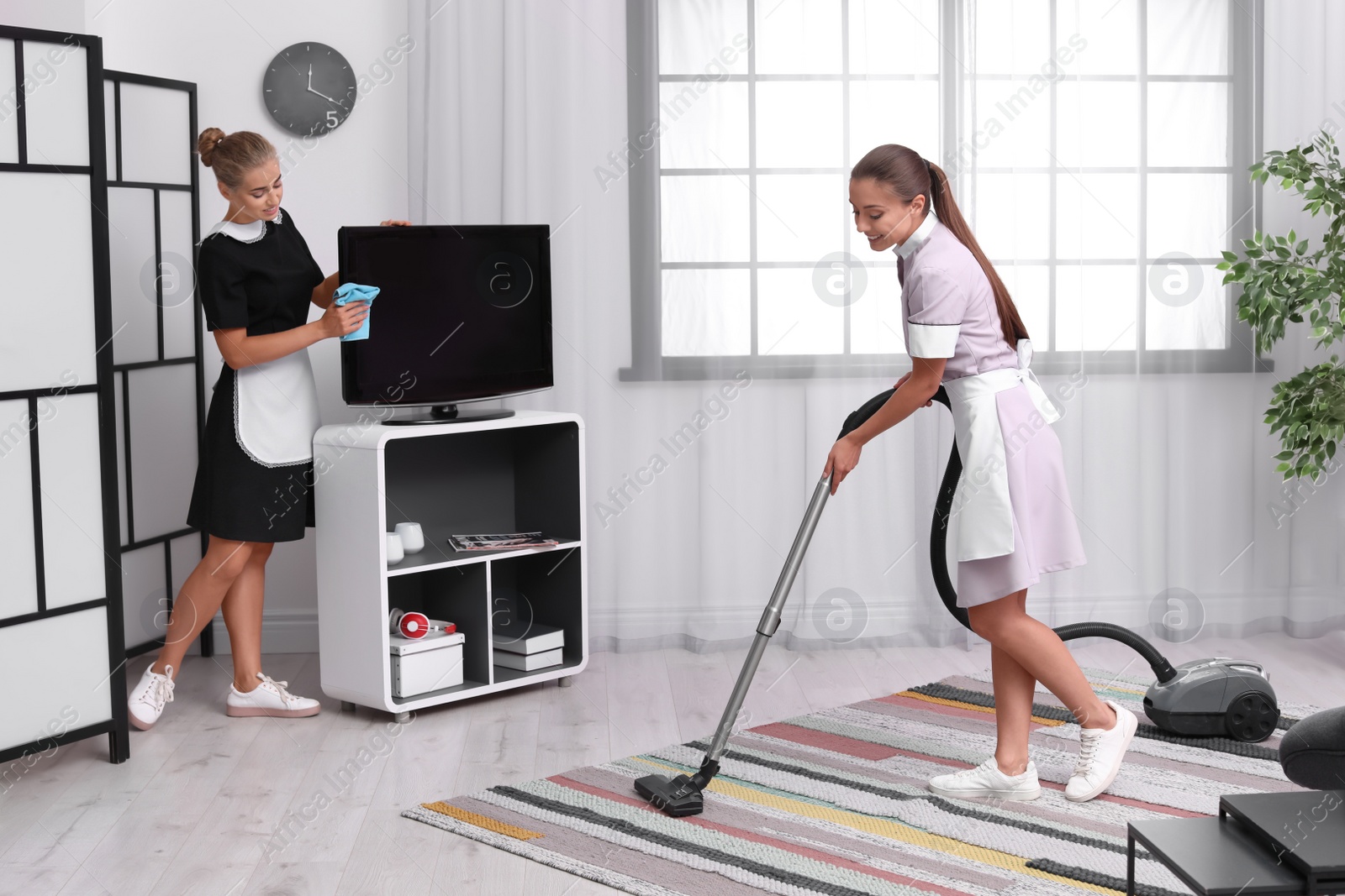 Photo of Professional chambermaids in uniform cleaning living room