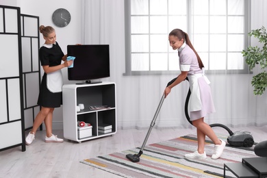 Photo of Professional chambermaids in uniform cleaning living room