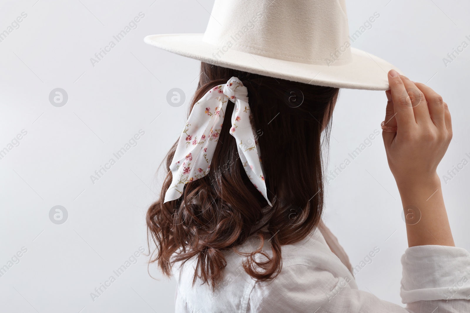 Photo of Young woman with hat and stylish bandana on light background, back view