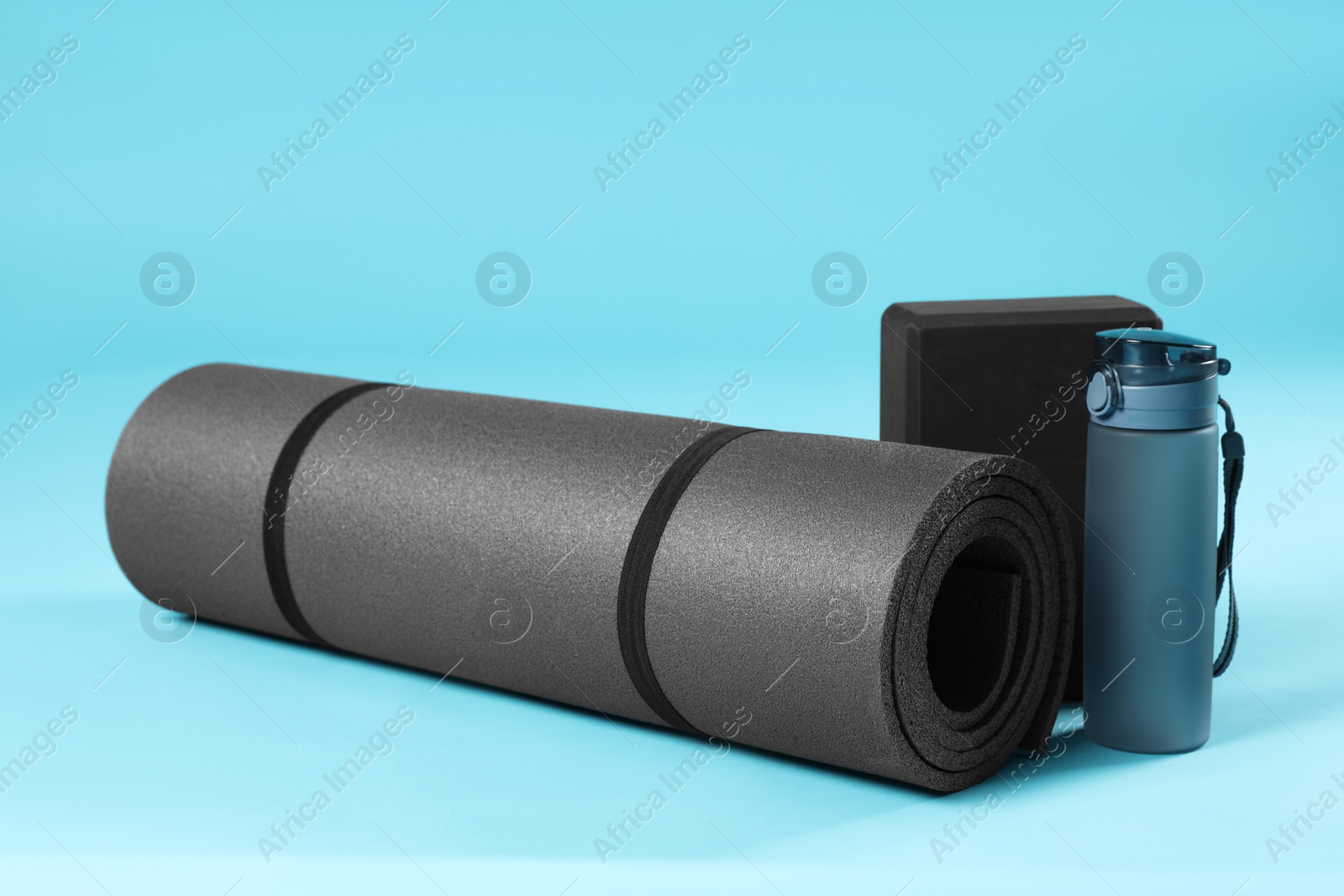 Photo of Exercise mat, yoga block and bottle of water on light blue background