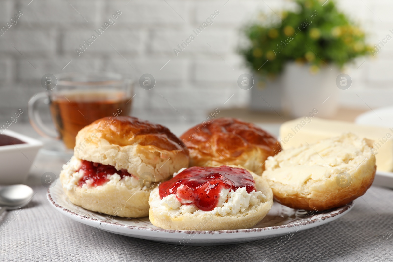 Photo of Freshly baked soda water scones with cranberry jam and butter on light grey mat, closeup