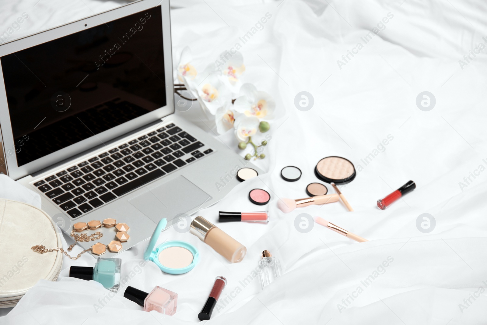 Photo of Composition with laptop and makeup products for woman on bed