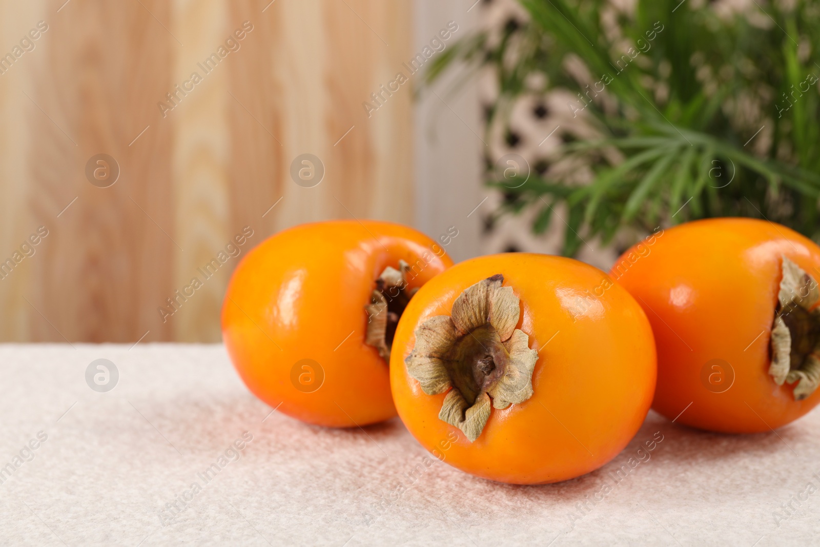 Photo of Delicious ripe persimmons on light textured table indoors, closeup. Space for text