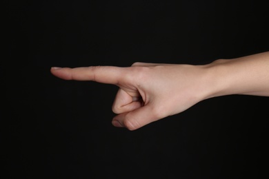 Woman pointing at something on black background, closeup. Finger gesture