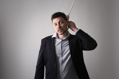 Photo of Depressed businessman with rope noose on neck against light grey background