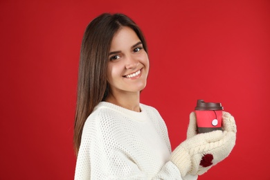 Happy beautiful woman with paper cup of mulled wine on red background