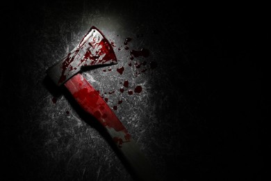 Axe with blood on dark gray textured surface in darkness, top view. Space for text