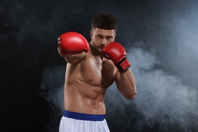 Photo of Man wearing boxing gloves fighting in smoke on black background