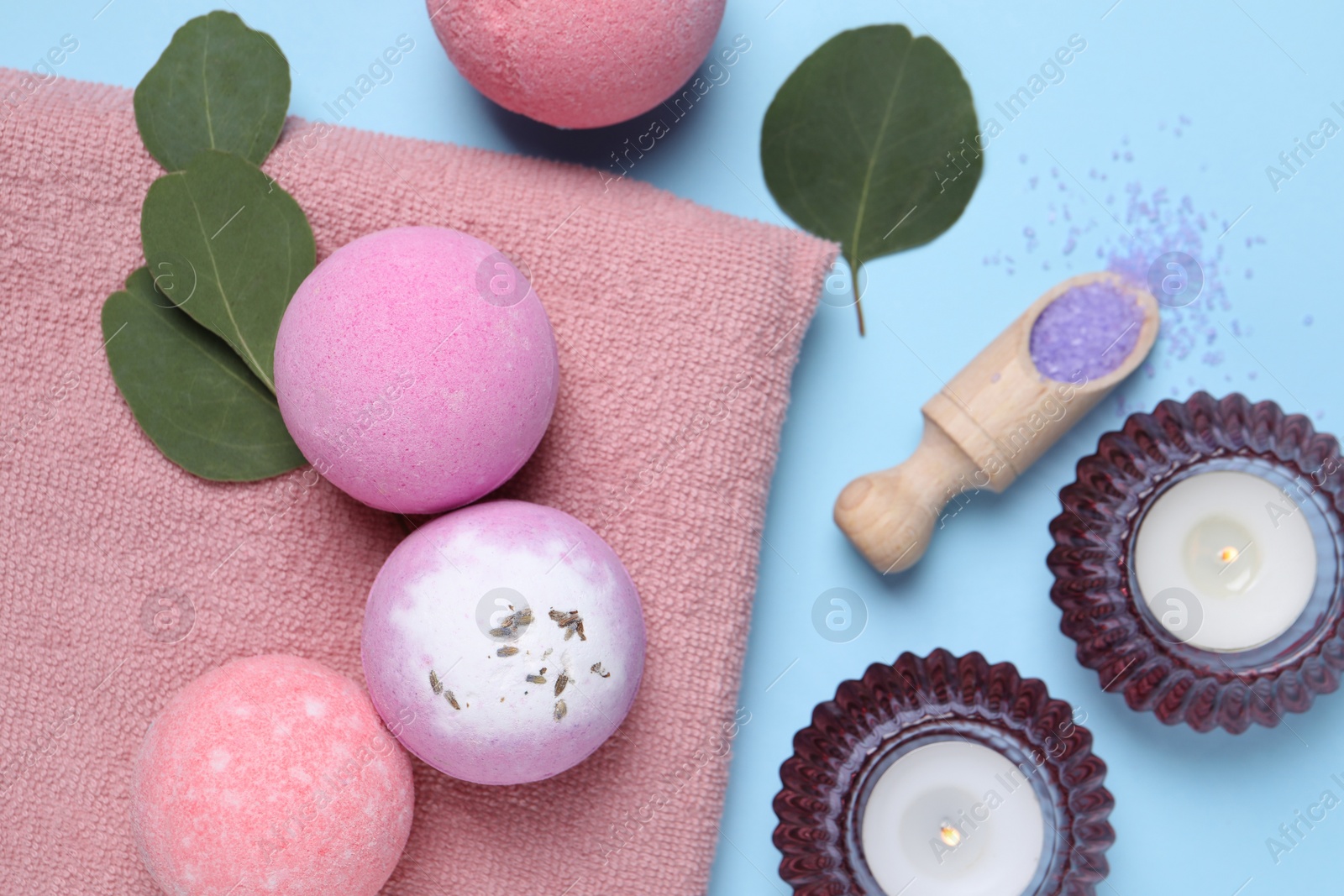 Photo of Bath bombs, eucalyptus leaves, burning candles and sea salt on light blue background, flat lay