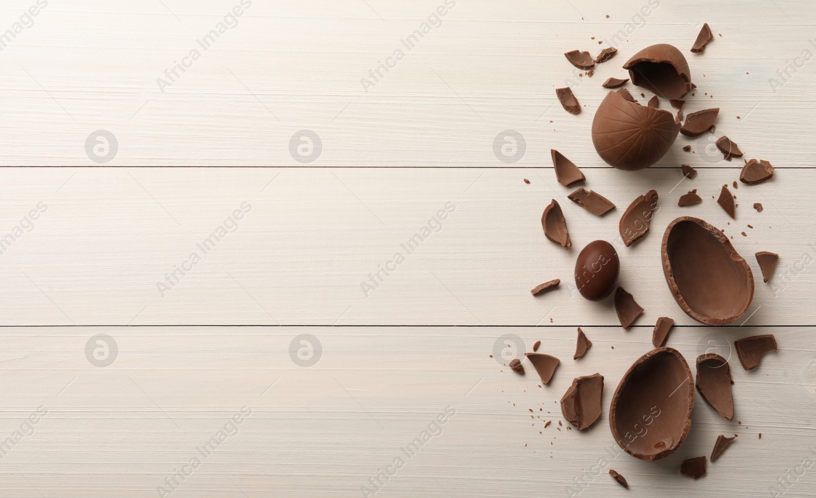 Photo of Broken and whole chocolate eggs on white wooden table, flat lay. Space for text