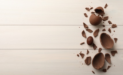 Photo of Broken and whole chocolate eggs on white wooden table, flat lay. Space for text