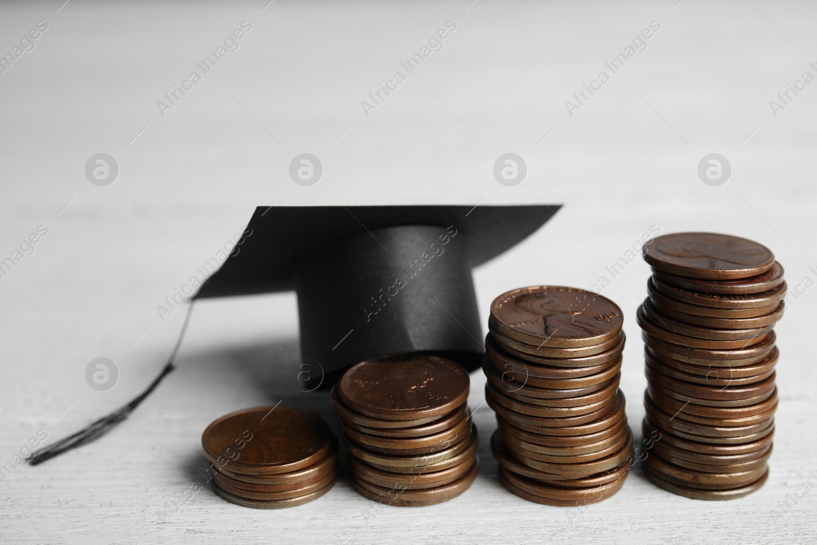 Photo of Coins and student graduation hat on white wooden background. Tuition fees concept