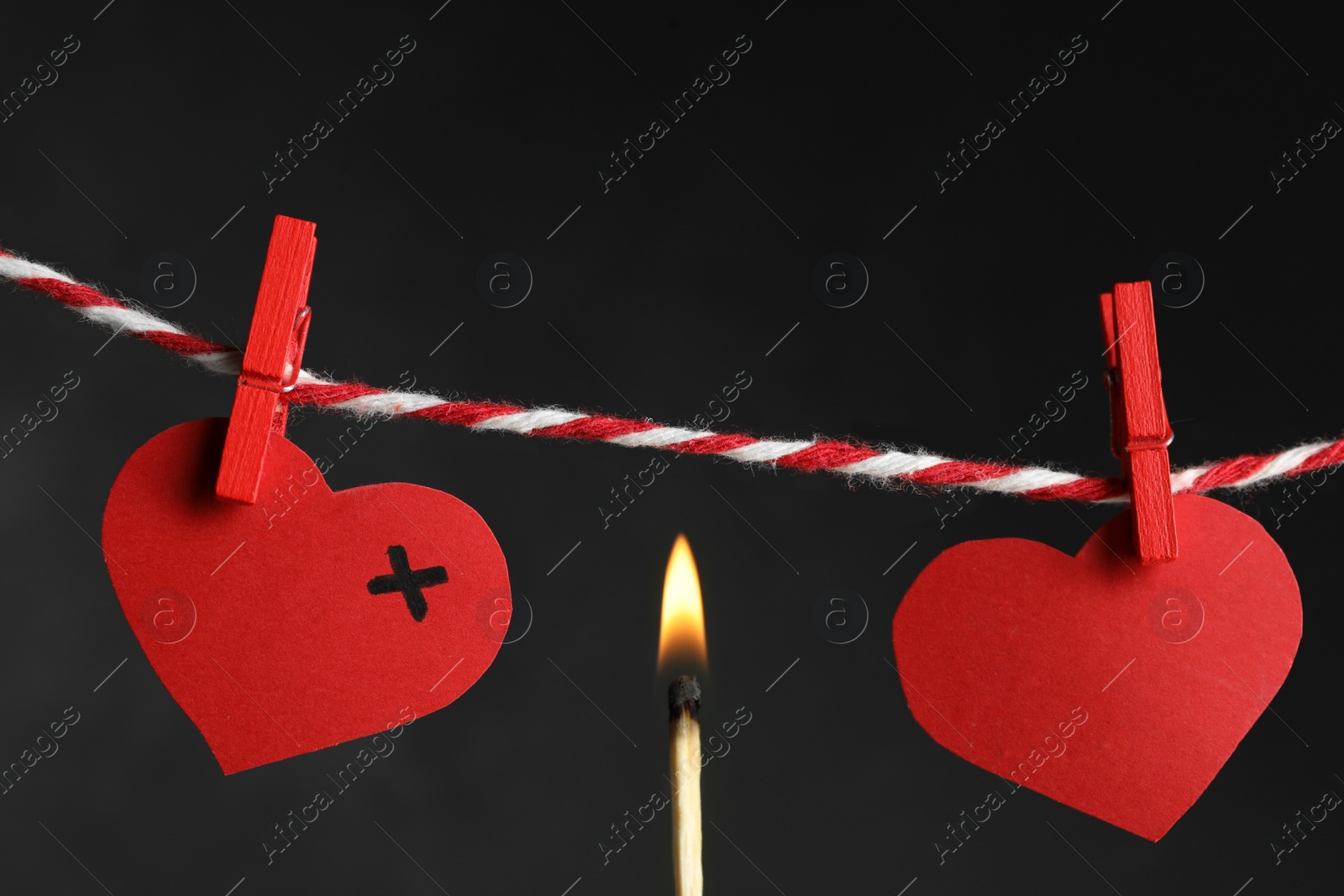 Photo of Red paper hearts on rope and burning match against black background. Composition symbolizing problems in relationship