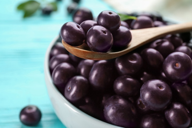 Photo of Tasty acai berries in bowl and spoon on table, closeup