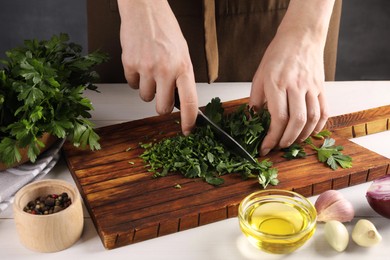 Woman cutting fresh parsley at white wooden table, closeup