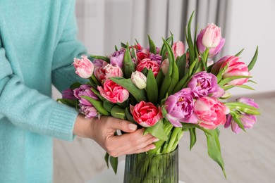 Photo of Woman putting bouquet of beautiful tulips in vase indoors, closeup