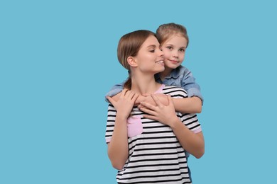 Photo of Little daughter hugging her mom on light blue background. Happy Mother's Day