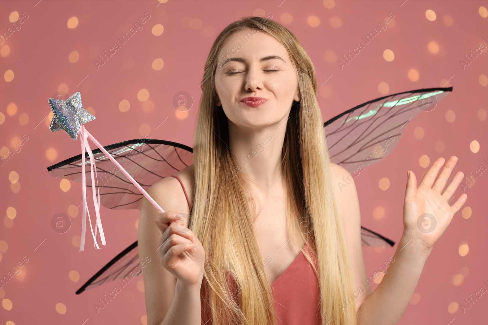 Photo of Beautiful girl in fairy costume with wings and magic wand on pink background