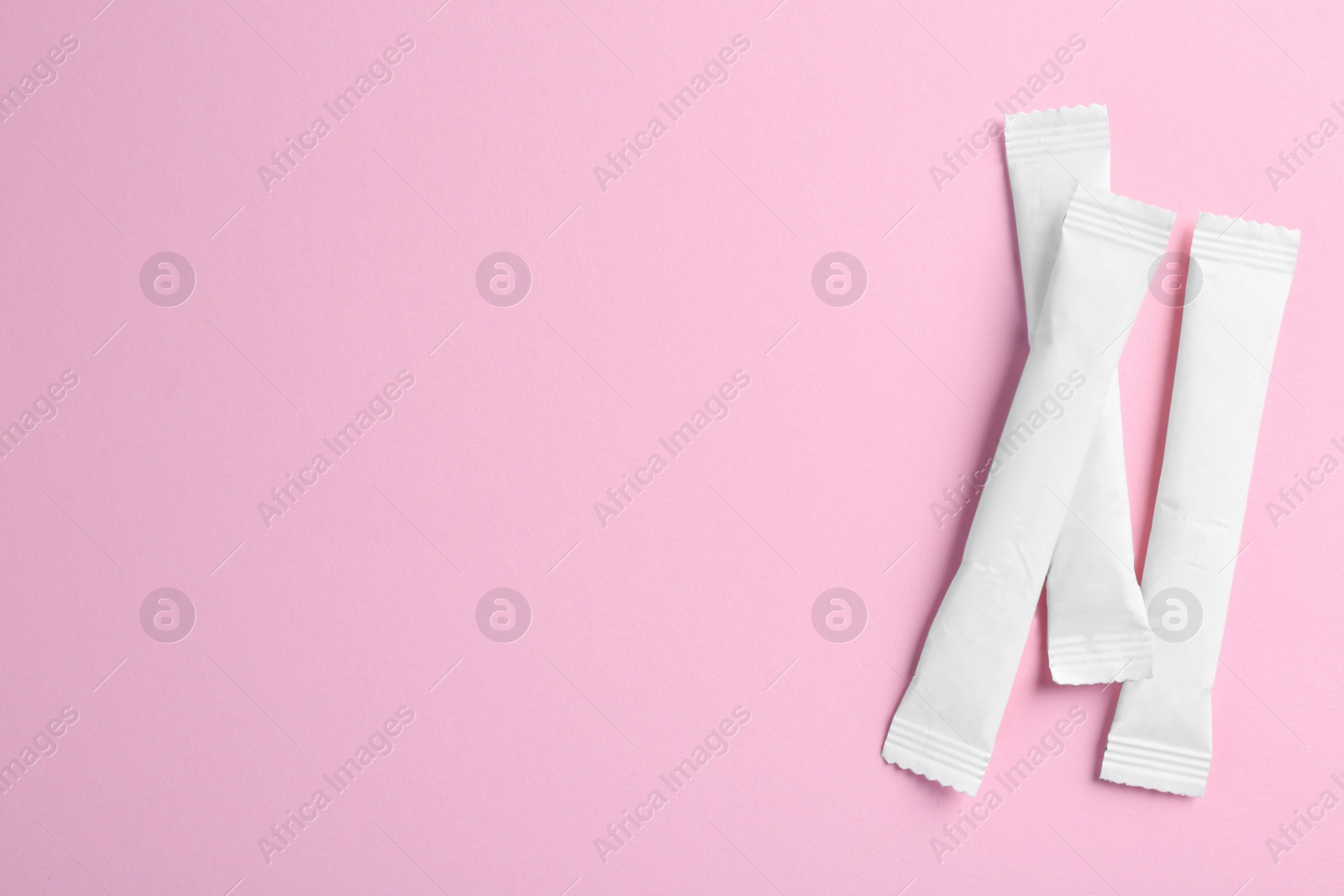 Photo of White sticks of sugar on pink background, flat lay. Space for text