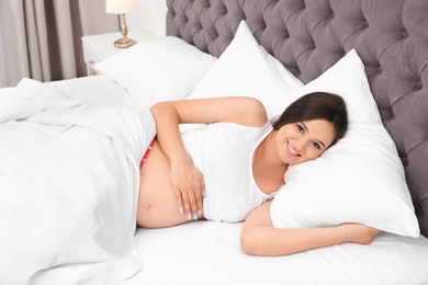 Photo of Beautiful pregnant woman lying on comfortable pillow in bed at home