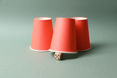 Photo of Three red cups and dice on pale olive background. Thimblerig game